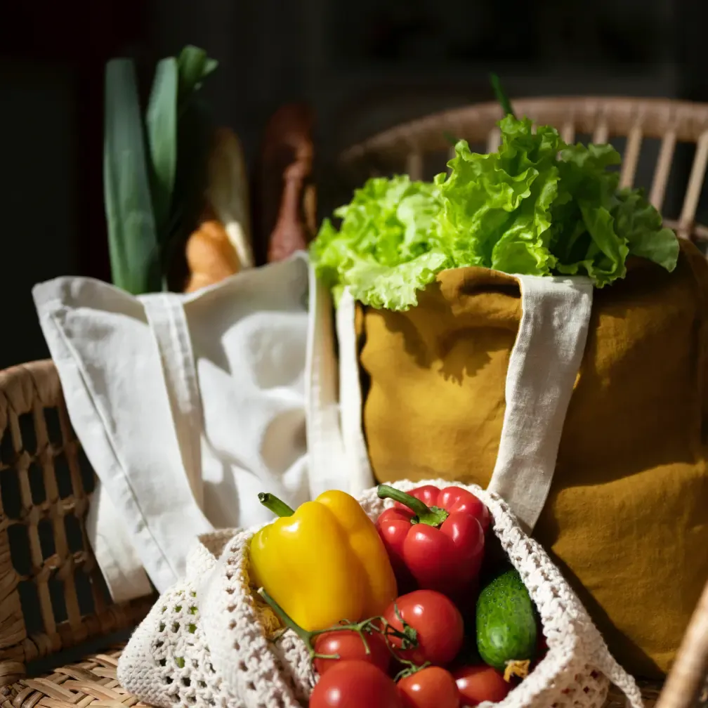 Lekkerland Fresh vegetables in reusable linen tote bags on wicker chair. Sustainable zero-waste grocery shopping, warm natural lighting